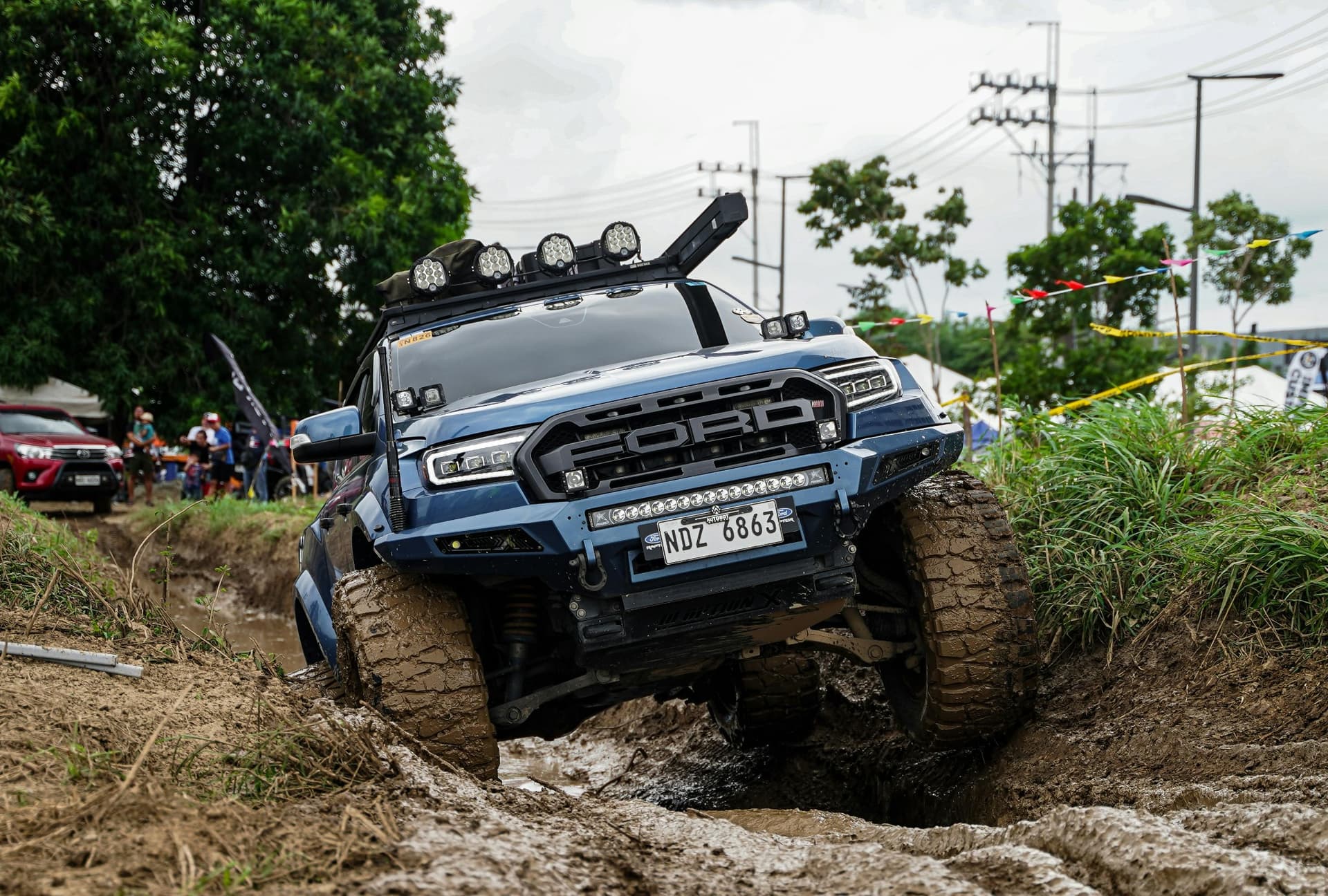 Ford Raptor flexing through a mud pit, fully modded with OZK suspension, lighting, and bumpers.