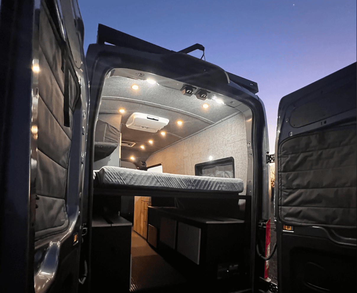Interior shot of a travel van with installed floor, lighting, and storage compartments.