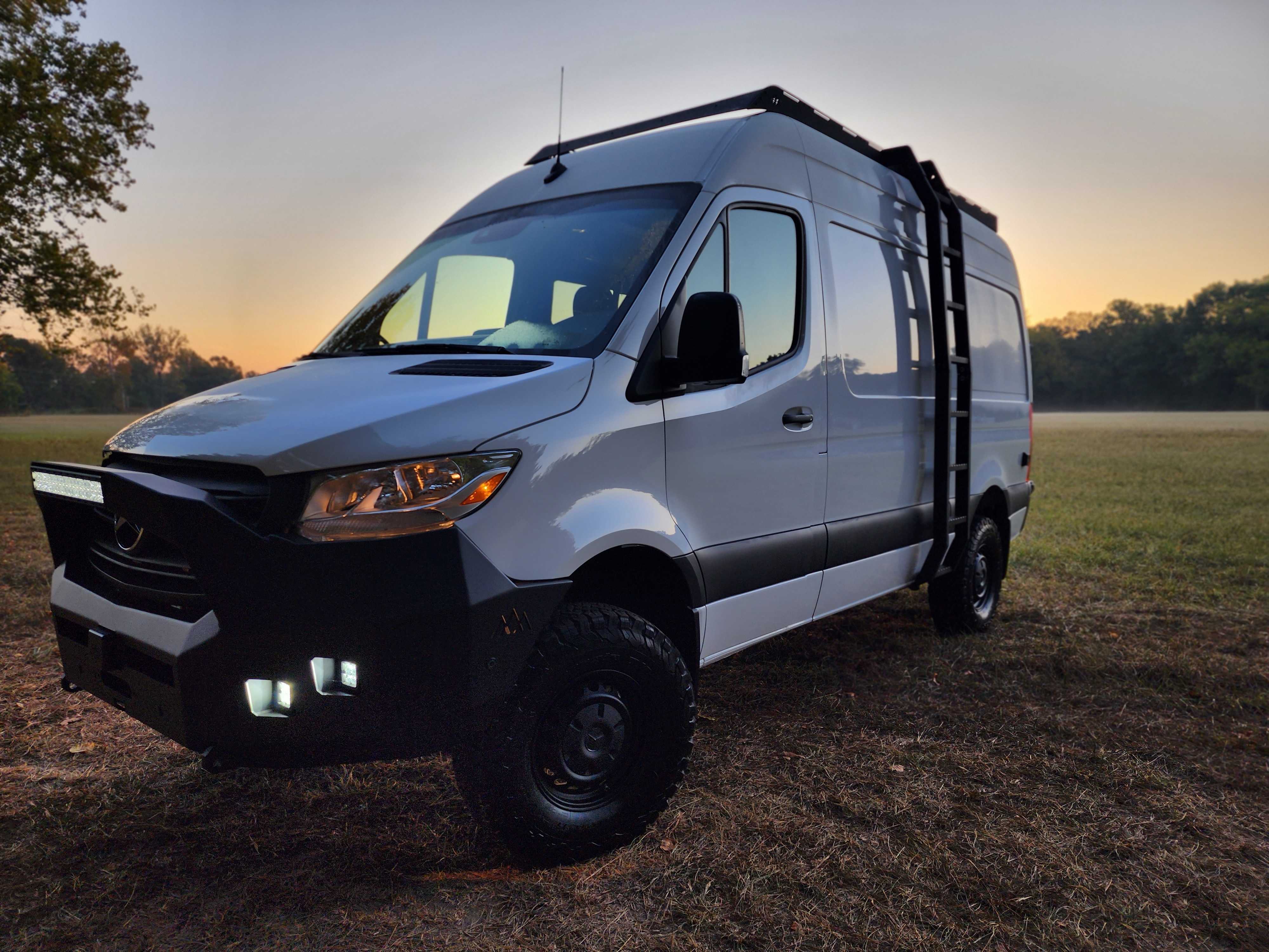 A custom camper van built by OZK Customs featuring full kitchen, pop-top roof, and modular sleeping system.